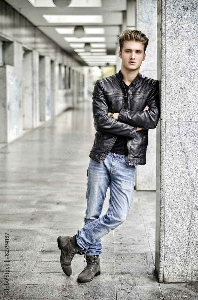 Young man with leather jacket standing outside against pillar Young man with leather jacket standing outside against pillar