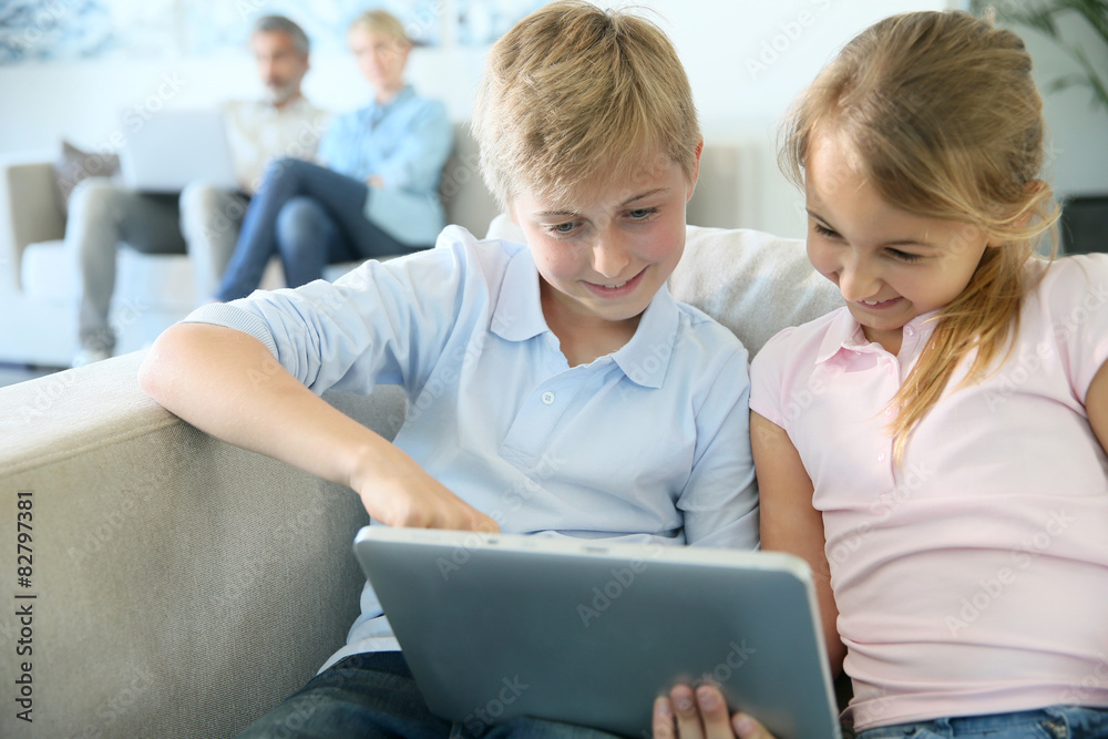 Kids using digital tablet at home, parents in background Kids using digital tablet at home, parents in background