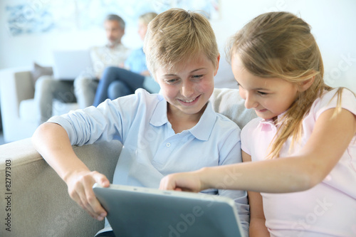 Kids using digital tablet at home, parents in background