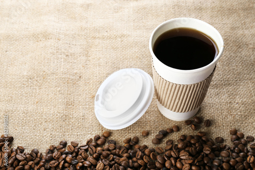 Paper cup of coffee with beans on sackcloth close up