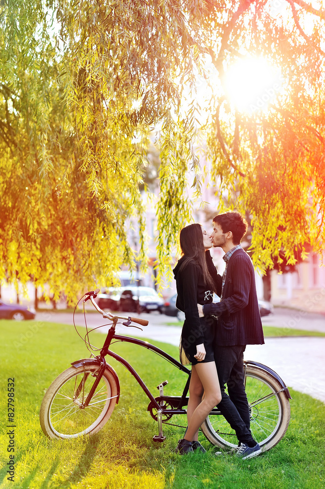 Obraz premium Young couple kissing in a park near a vintage bike