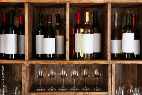 Shelving with wine bottles with glasses on wooden wall background