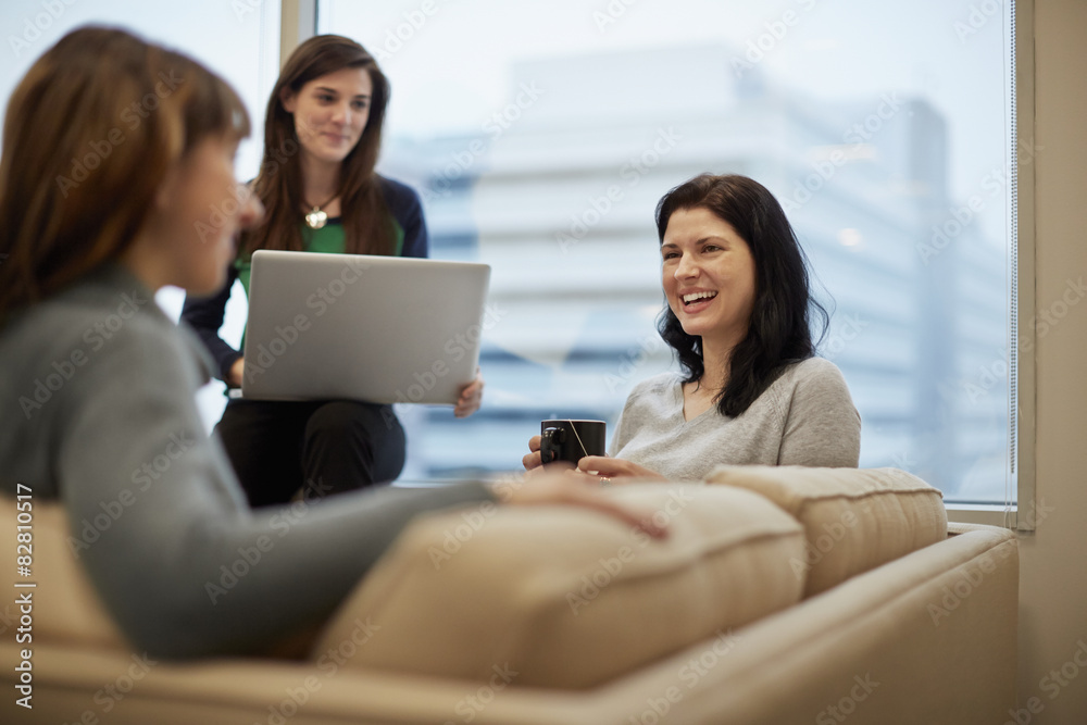 Three businesswomen by a window in an office, one holding a laptop. Three businesswomen by a window in an office, one holding a laptop.