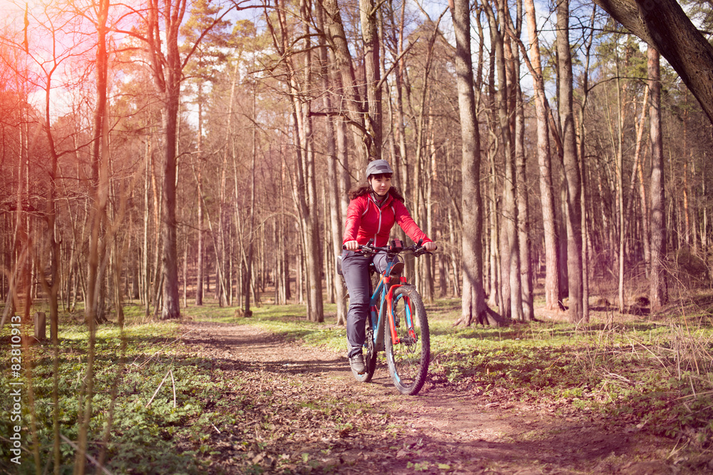 Fototapeta premium Young woman riding a bicycle through forest