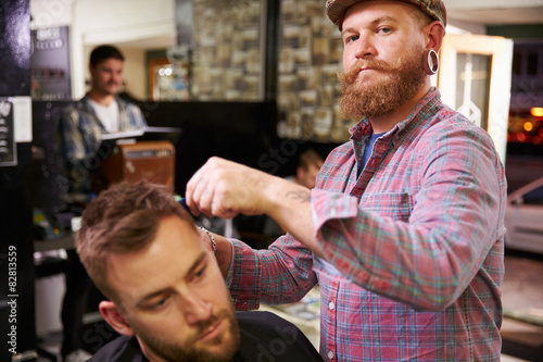 Portrait Of Male Barber Giving Client Haircut In Shop