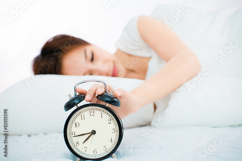 Woman in bed trying to wake up with alarm clock