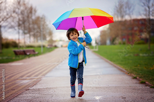 Cute little boy, walking in a park on a rainy day, playing and j