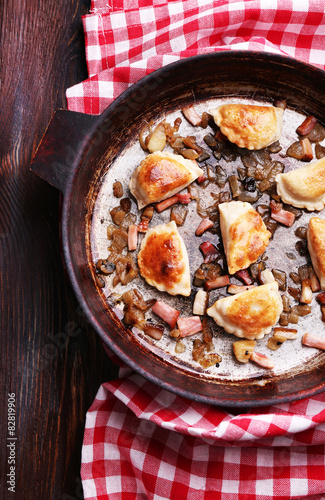 Fried dumplings with onion and bacon in frying pan, on wooden table background