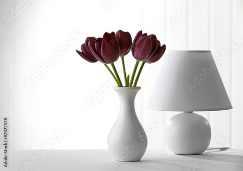 Beautiful violet tulip in vase with lamp on light background