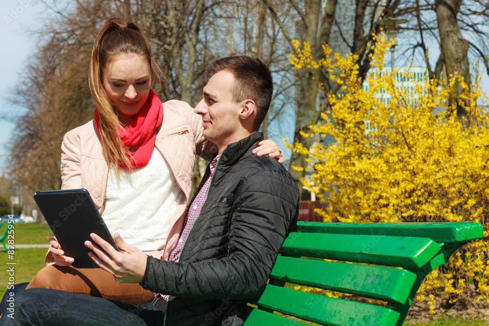 Fototapeta premium couple with tablet sitting on bench outdoor
