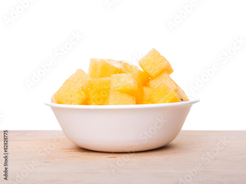 Yellow watermelon fruit in white bowl on wooden cutting board