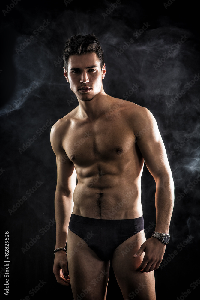 Handsome, fit young man wearing only underwear standing on black
