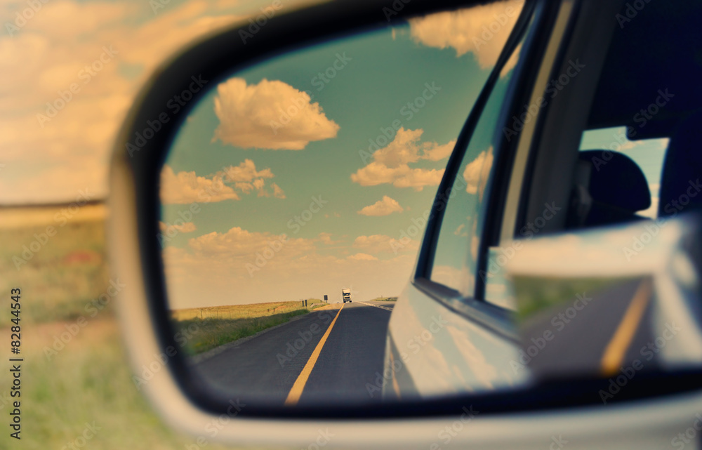 Rear view mirror and long road through arid landscape 