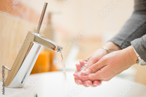female is washing hands with tap water in bathroom, shallow dept