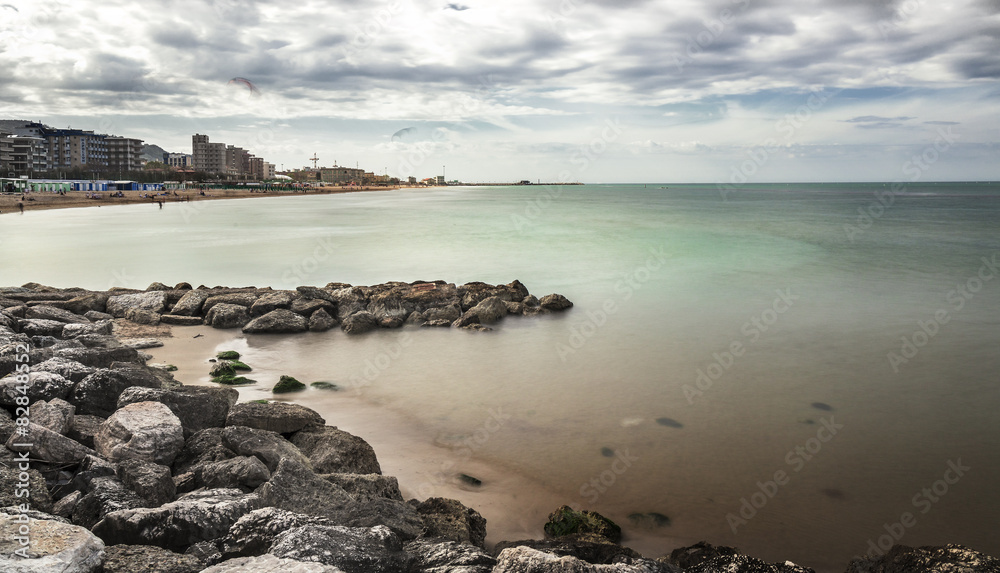 Long exposure warm sea and rocks with beach and city background.