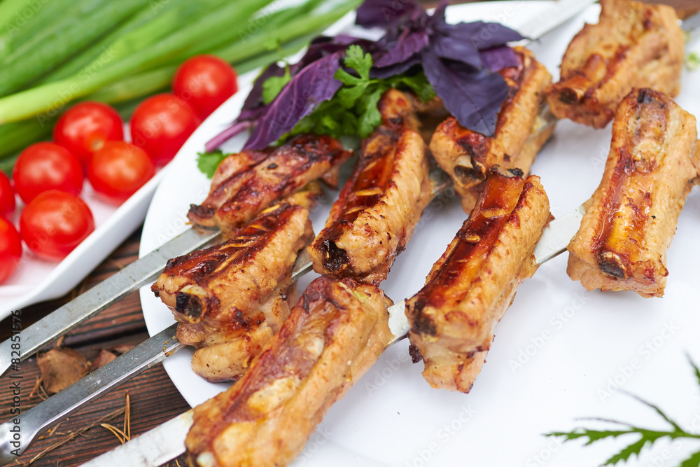 Three skewers with grilled ribs lie on a white plate with cherry