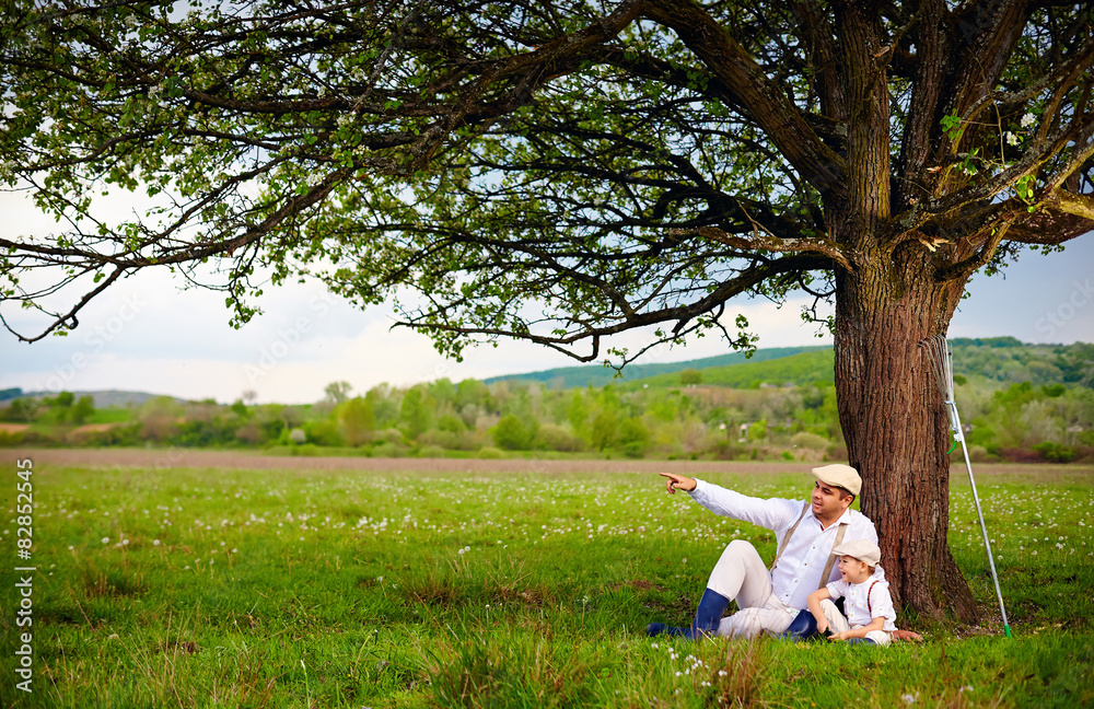 farmer father and son sitting under the tree, spring countryside farmer father and son sitting under the tree, spring countryside