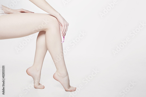 Woman shaves her slim long legs with razor.