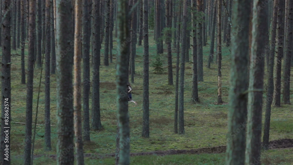 Young wild girl running through the dark pine forest. Pan shot Young wild girl running through the dark pine forest. Pan shot