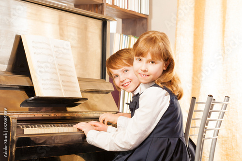 Two cute small girls in uniforms playing piano