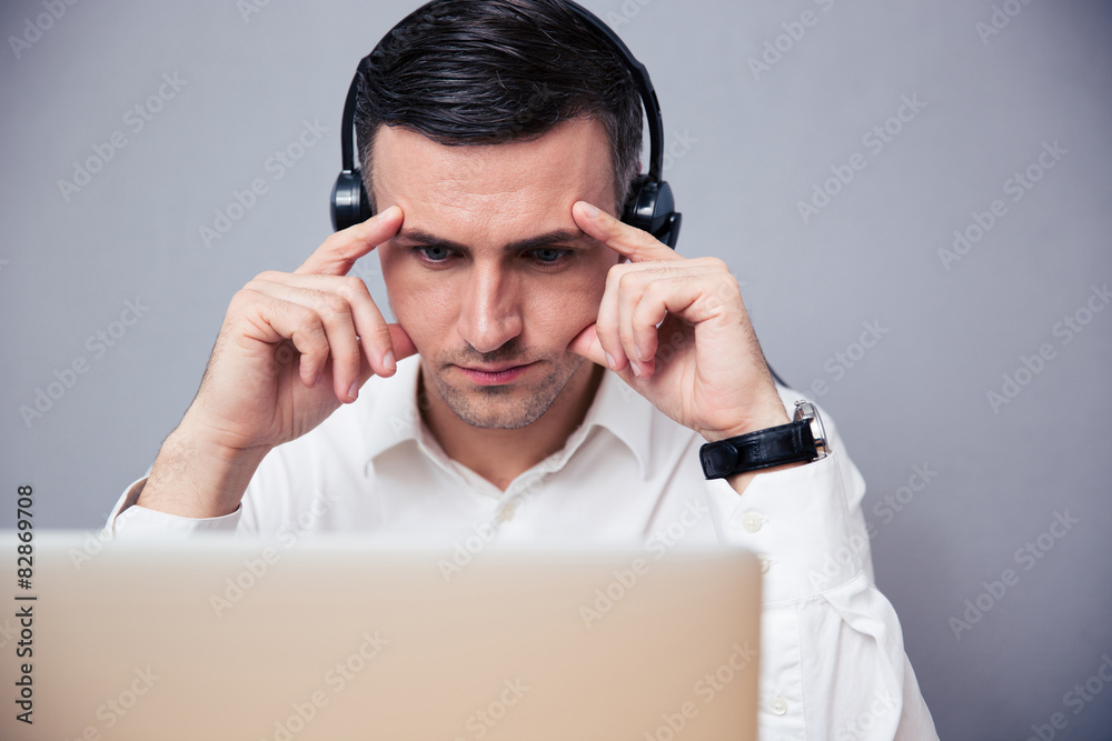 Pensive businessman working on laptop with headphones Pensive businessman working on laptop with headphones