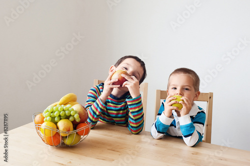 Two boys sitting at the table and eating apples