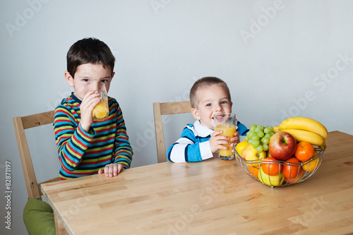 Two boys sitting at the table and drinking orange juice