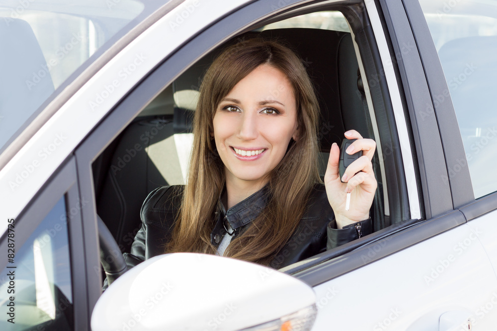 Young smiling woman in car with key in hand.