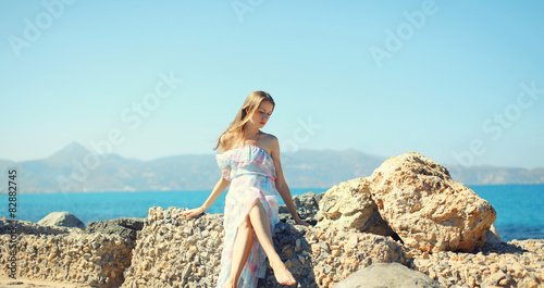 Beautiful young woman in dress siting on stone against the sea, © rohappy
