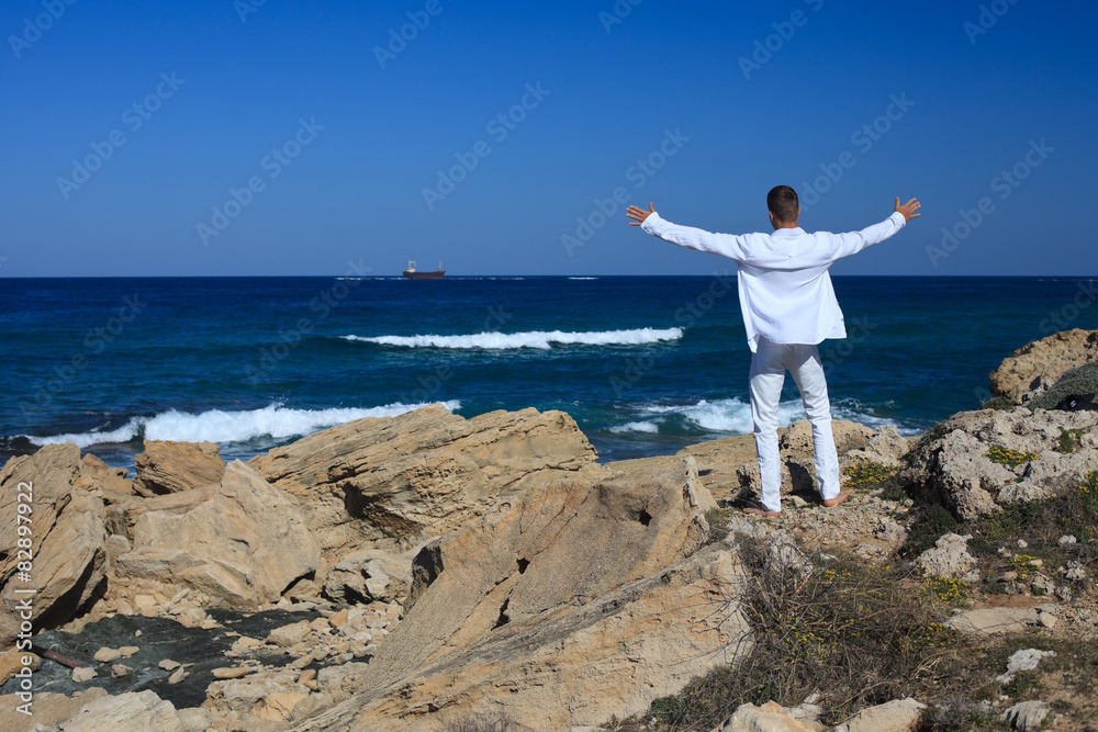 man is standing arms spread on a rock near the sea