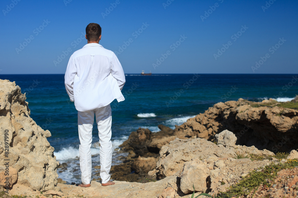 young man standing on a rock and looking at sea