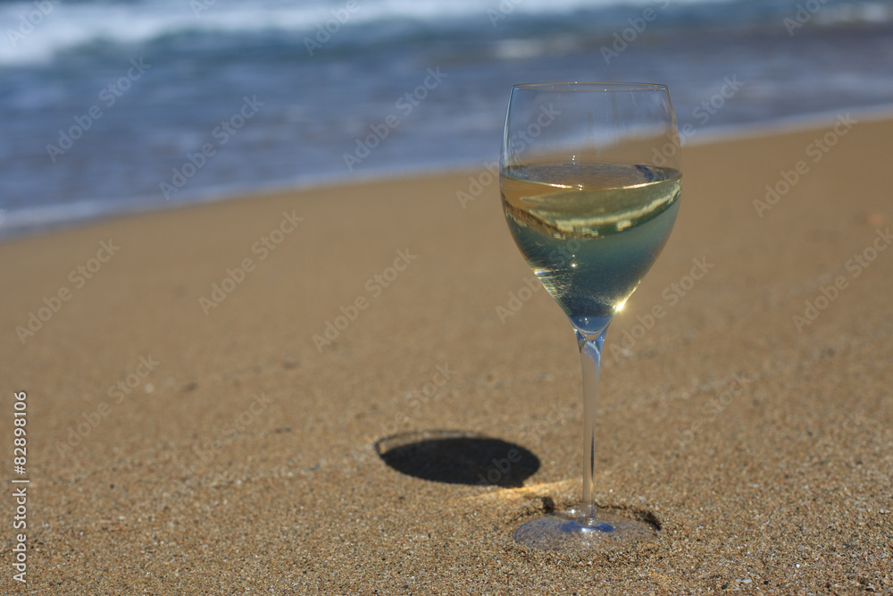 A glass of white wine in the sand on the beach. Horizontal
