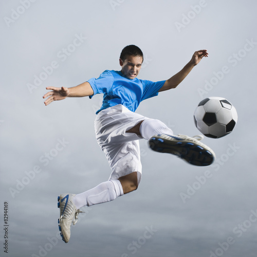 Mixed race teenager in mid-air kicking soccer ball photo