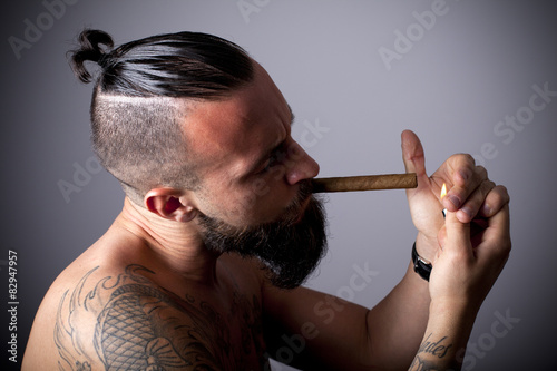 Joven hipster con tatuajes encendiéndose un puro photo