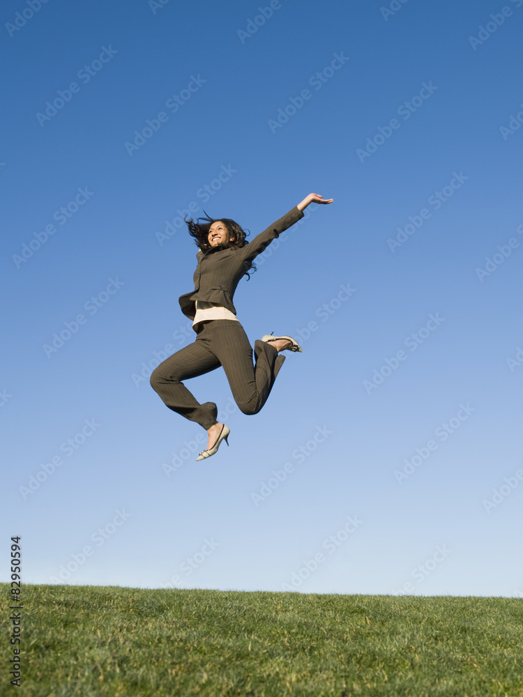 Mixed race businesswoman jumping in field Mixed race businesswoman jumping in field