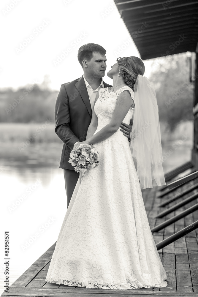 Black and white shot of bride and groom posing on pier at river