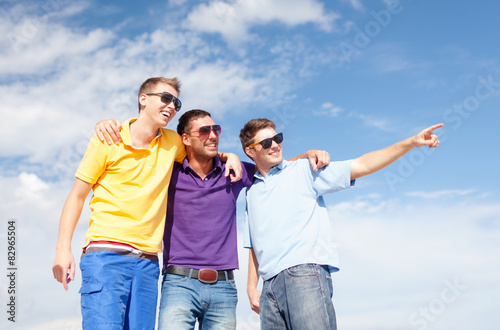 smiling friends in sunglasses pointing finger