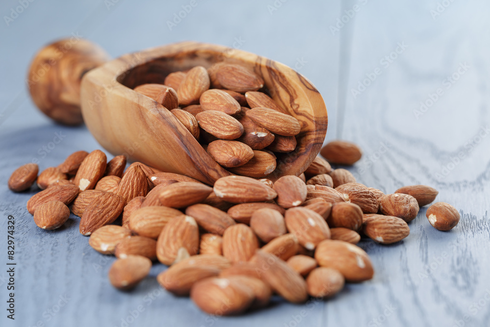 roasted almonds in measuring scoop on blue wooden table