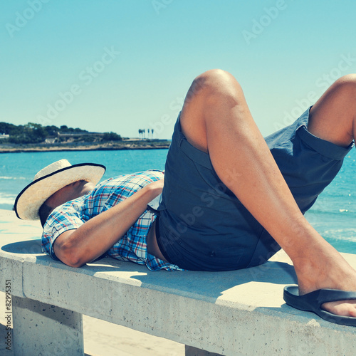 young man lying down in a street bench near the sea
