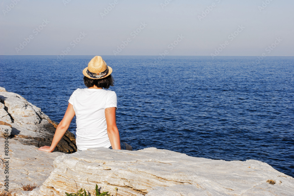 Girl in straw hat watching at the sea