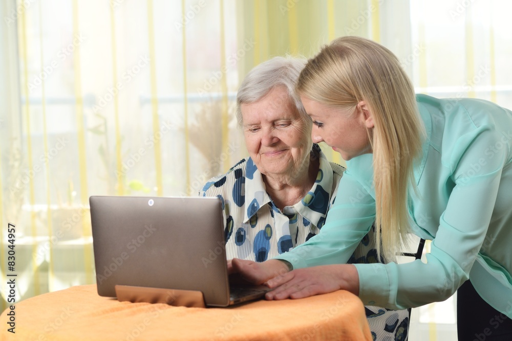Senior woman with her caregiver in home using laptop.