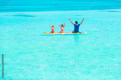 Little girls and young dad on surfboard during summer vacation