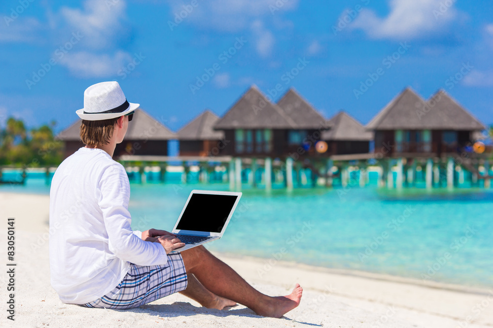 Naklejka premium Young man with laptop at tropical beach near water villa