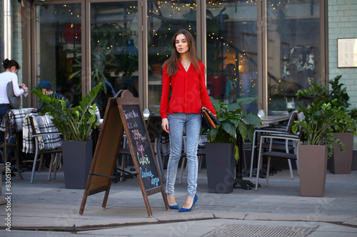 Young beautiful girl in jeans and a red blouse is walking down t