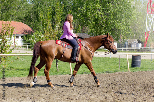 young smiling girl riding her brown horse in a training field