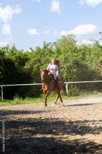 young smiling girl riding her brown horse in a training field