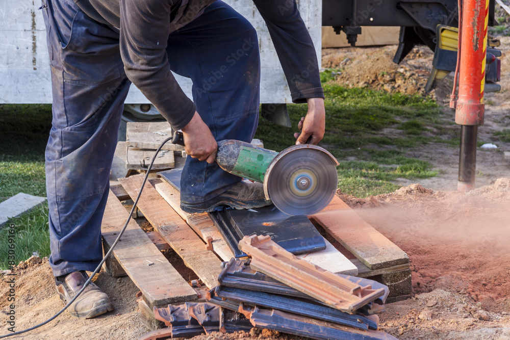 Worker using a hand circular saw to cut a roof-tile Worker using a hand circular saw to cut a roof-tile