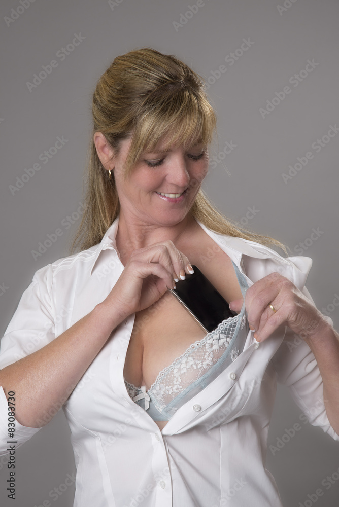Woman putting mobile phone into her bra for safe keeping Stock
