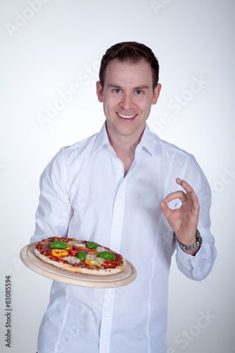 Mann serviert lächelnd eine Pizza und zeigt OK Porträt