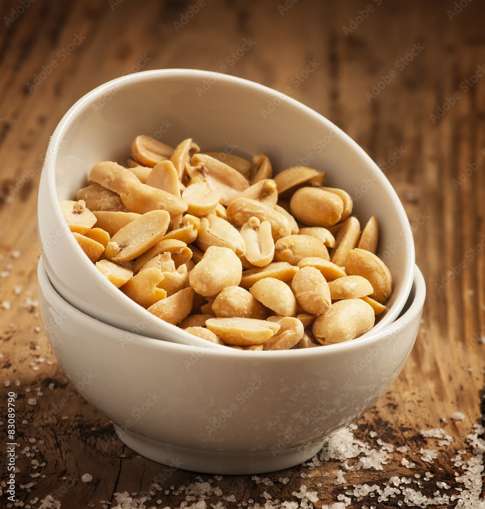 Roasted peanuts and salt in a bowl on a wooden background, selec